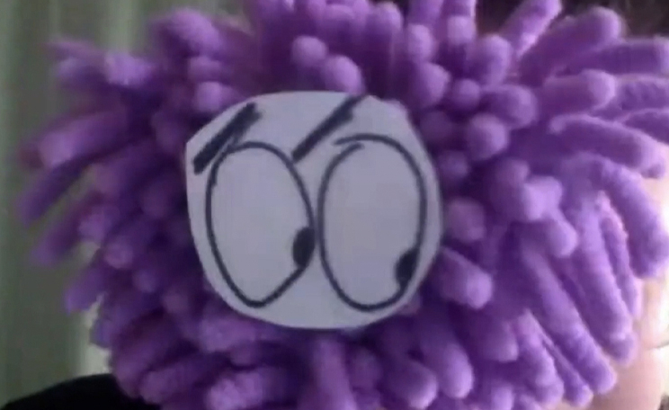 Teaching Artist holding up fuzzy purple puppet that has eyes looking down.