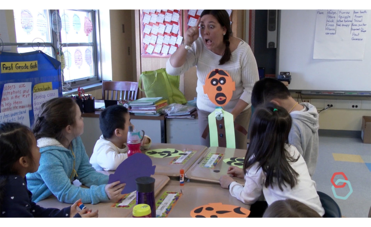 Teacher making her face match the expression of her puppet's face to a group of students.