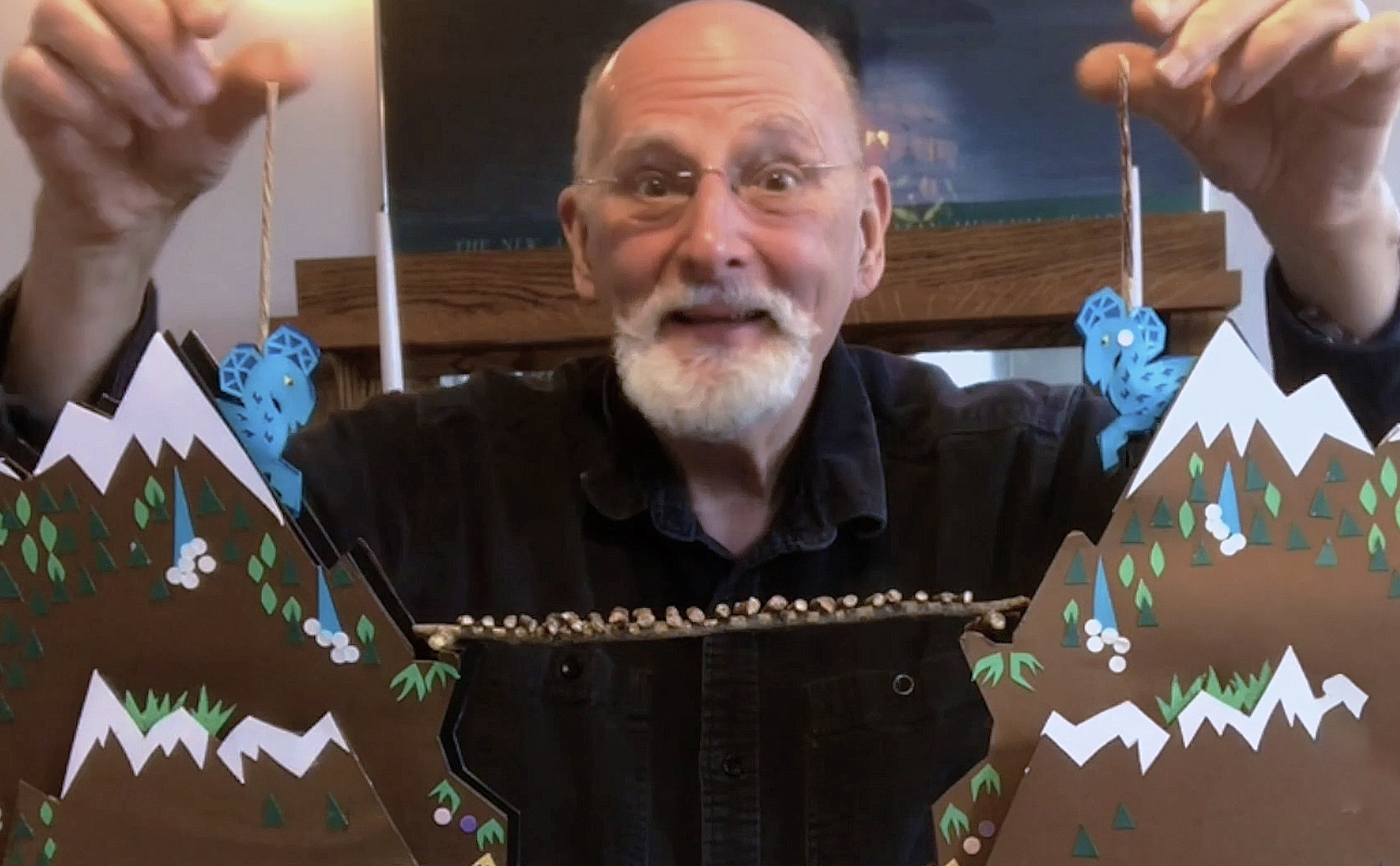 Teaching artist Ron Sopyla showing his table top puppet set up holding up two goat puppets, each one on its own mountain on either side of his table with a bridge in between.