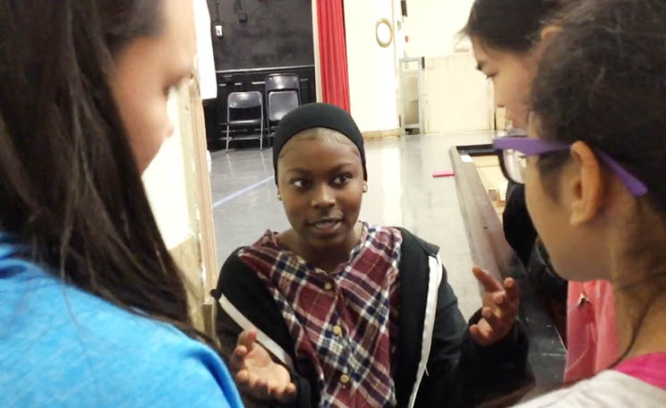 a student with dark brown skin and a plaid shirt speaks to their peers