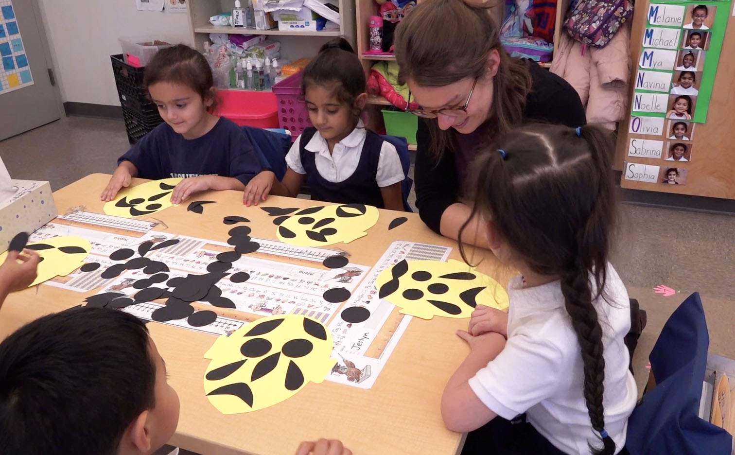Educator leans in close to a table of kids with their art projects on the table.