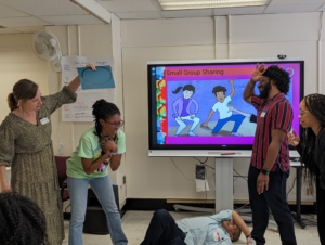 Teachers pose in a tableaux facilitator holds a speech bubble above one teacher's head