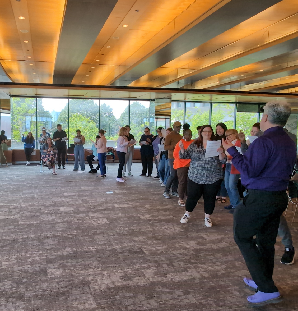 Teachers-stand-in-a-large-circle-holding-music-paper-in-their-hands-working-in-small-groups