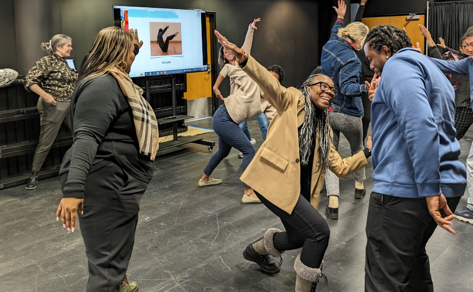 a dance teachers smiling makes a shape in front of participant