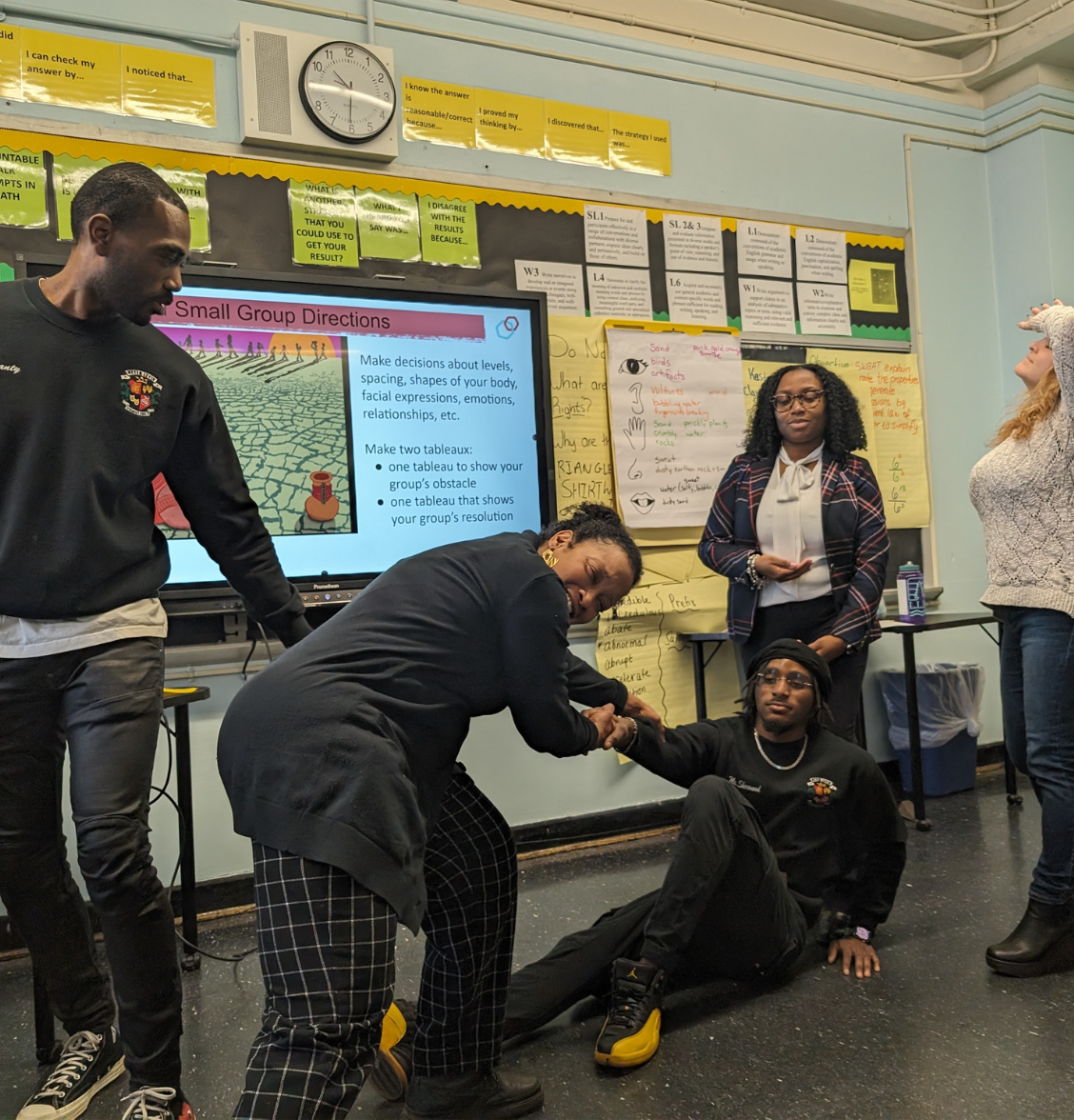 a group of teachers make a tableau inspired by a long walk to water.. One person is being pulled another is looking back, and one person has their hand on their head.